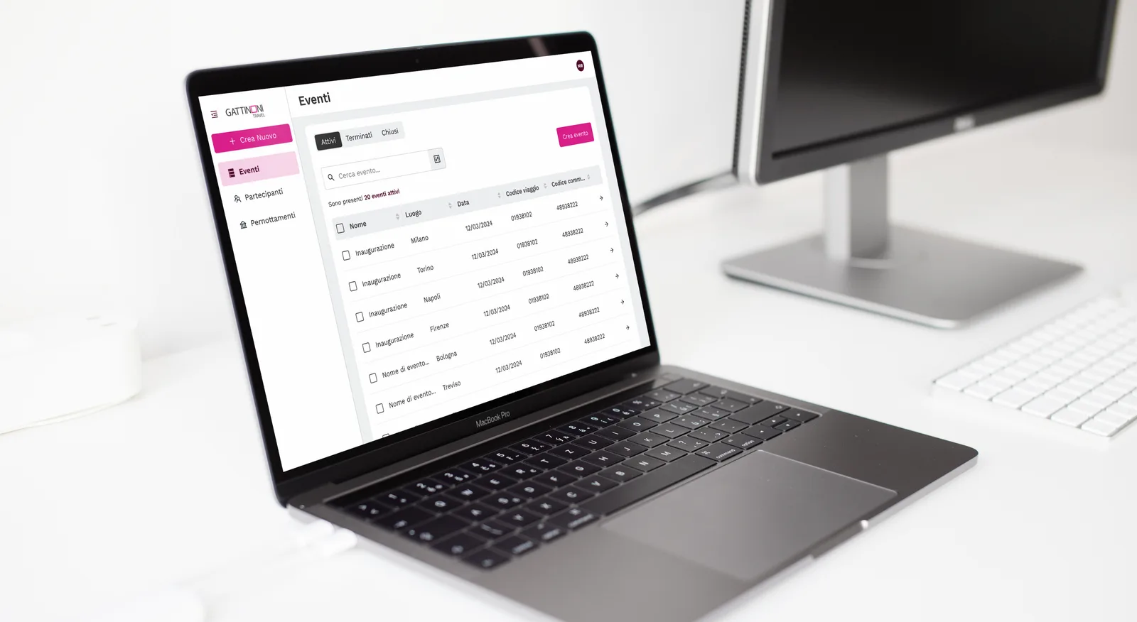 Un MacBook Pro su una scrivania bianca mostra la lista Eventi della piattaforma: una sidebar con Eventi, Partecipanti e Pernottamenti accanto a una tabella di venti eventi attivi con luogo, data, codice viaggio e codice commessa.