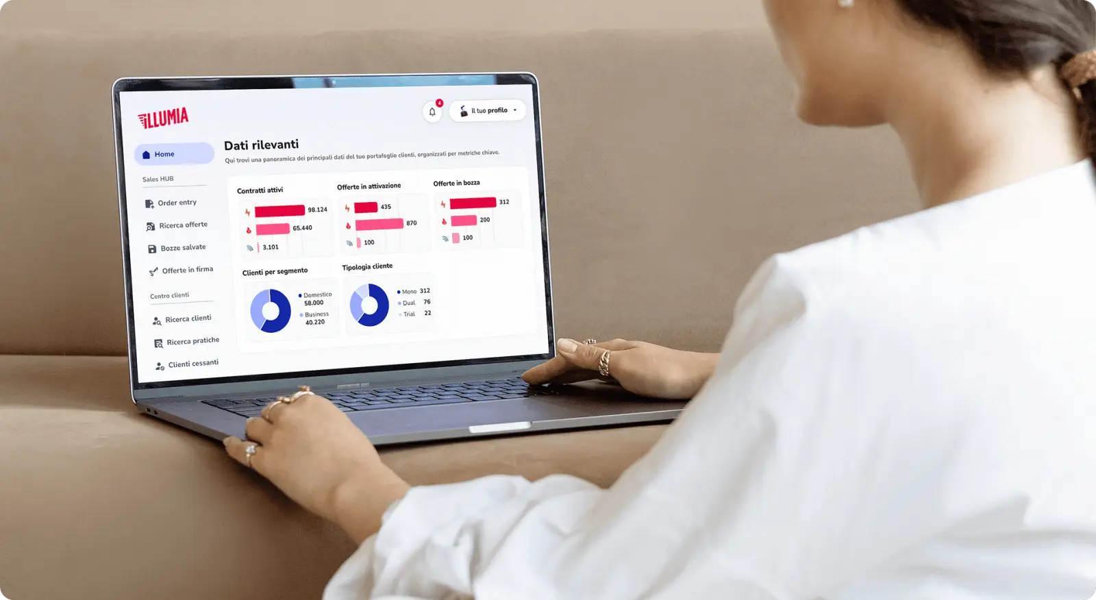 A woman working on a laptop showing the Illumia agent portal dashboard with contract and client charts.