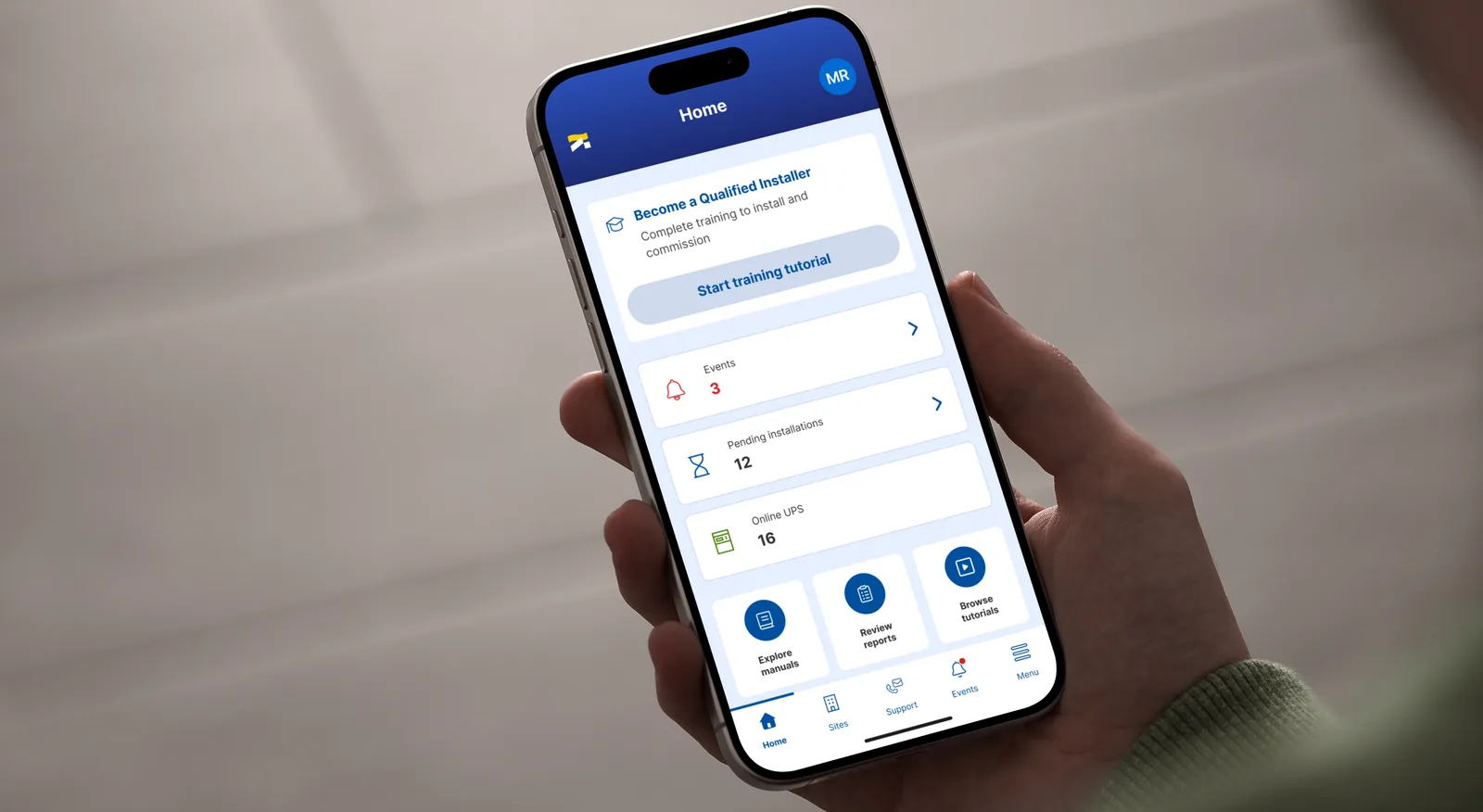 A hand holding a phone with the Socomec app home screen: an installer training card above counters for events, pending installations and online UPS units.